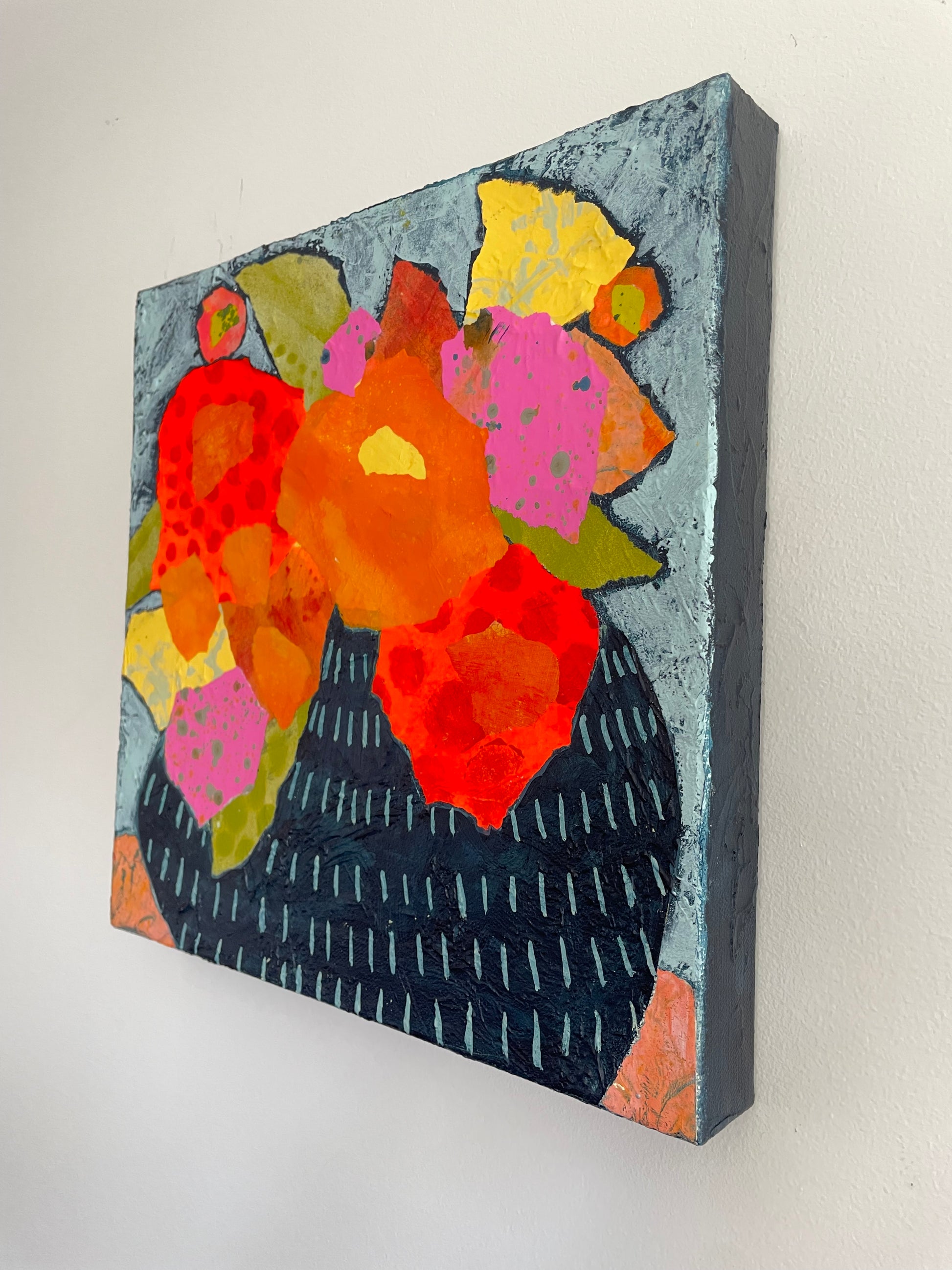 Close view of abstract floral painting showing layered painted paper flowers in pink and yellow with visible texture and collage edges