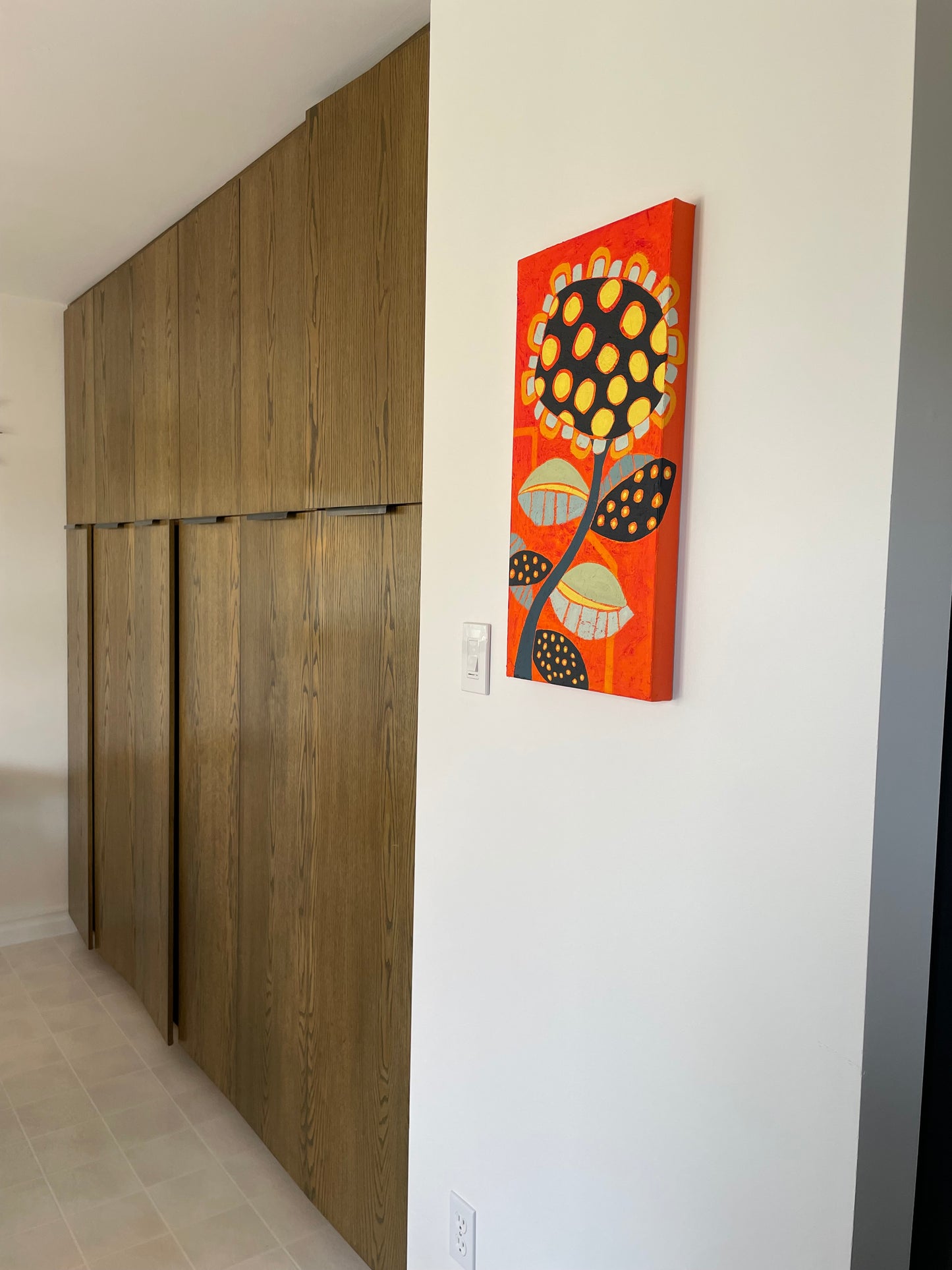 Abstract floral wall art in orange, black, and yellow displayed in a neutral interior as a bold focal point